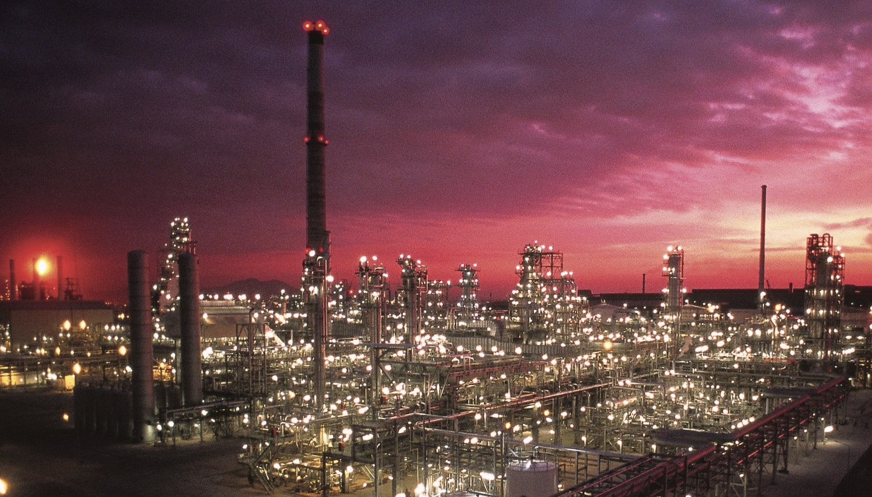 A lit oil refinery with a sunset behind